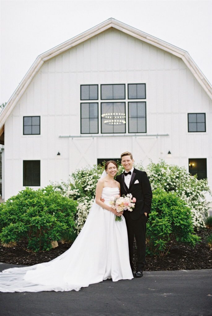couple smiling in front of barn outside at a wedding venue in door county